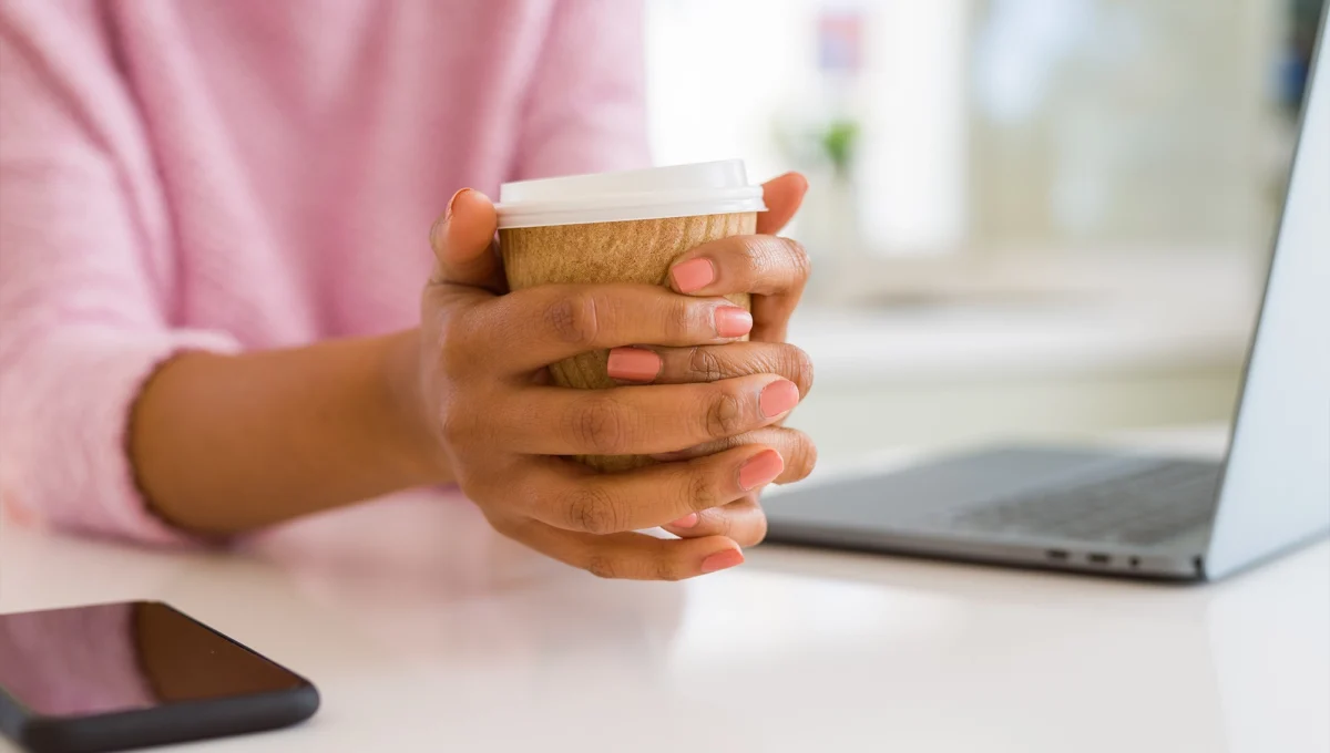 Close up of young woman drinking a coffee while working using laptop